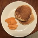 Two pancakes and cantaloupe slices on a plate.